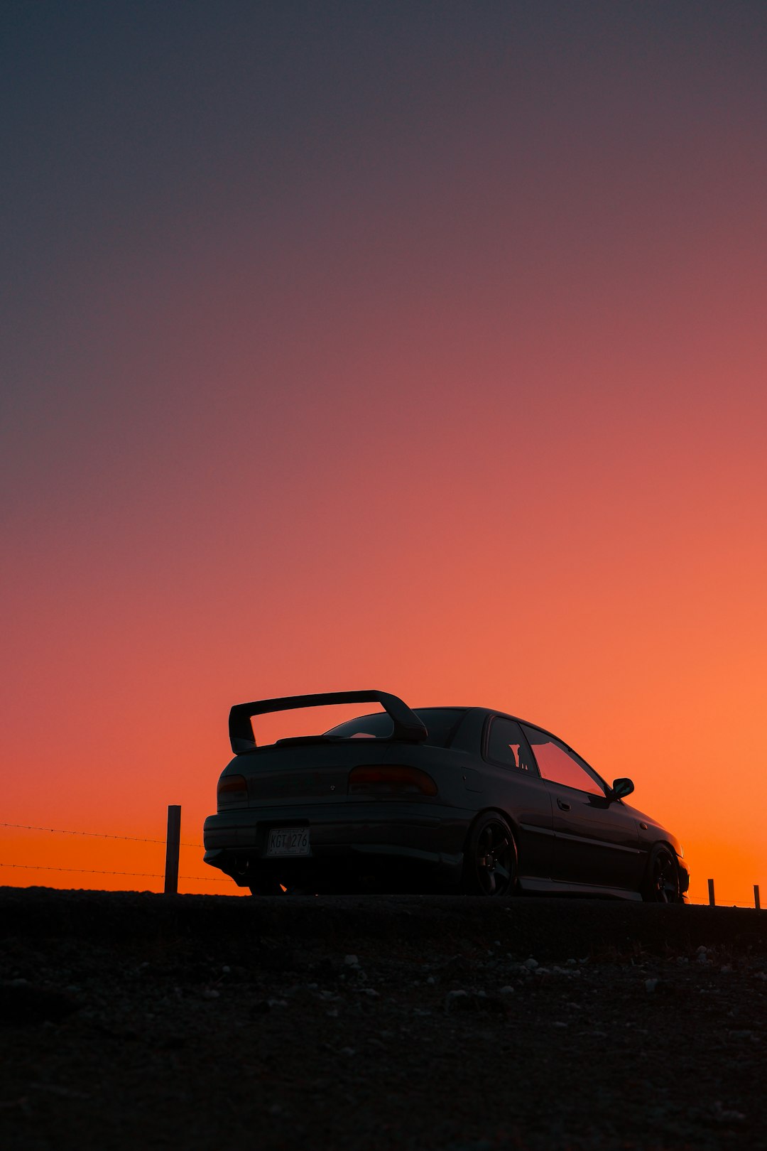 Sports car silhouetted against a vibrant sunset sky