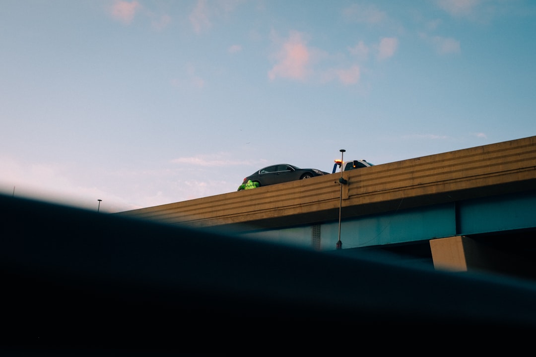 Two cars drive on a bridge under a cloudy sky