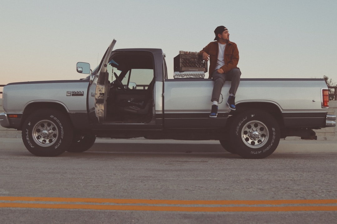 man in white t-shirt and black pants standing beside white crew cab pickup truck