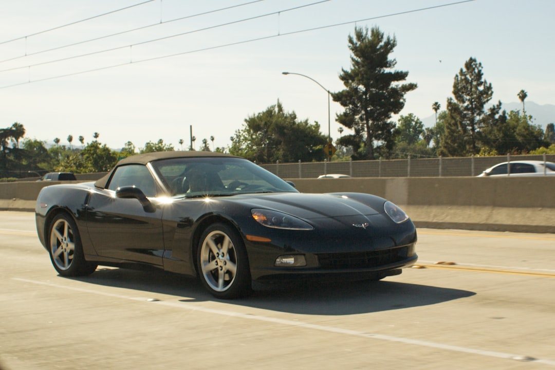 A black convertible corvette drives on a sunny highway