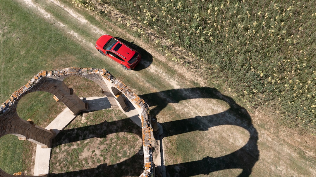 Red car driving on dirt road near ruins