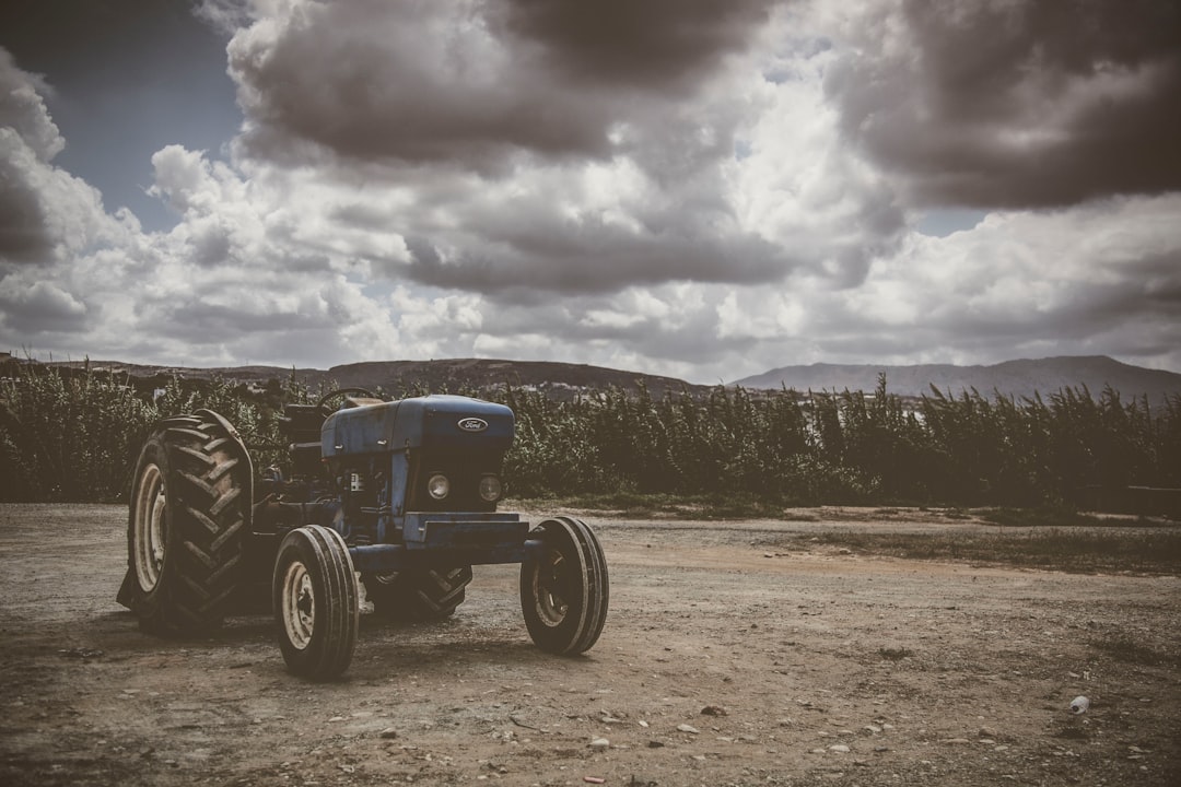 blue tractor near green field under dramatic clouds during daytime