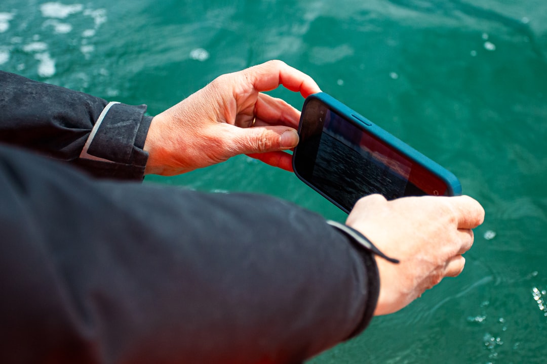 Hands holding a smartphone above green water