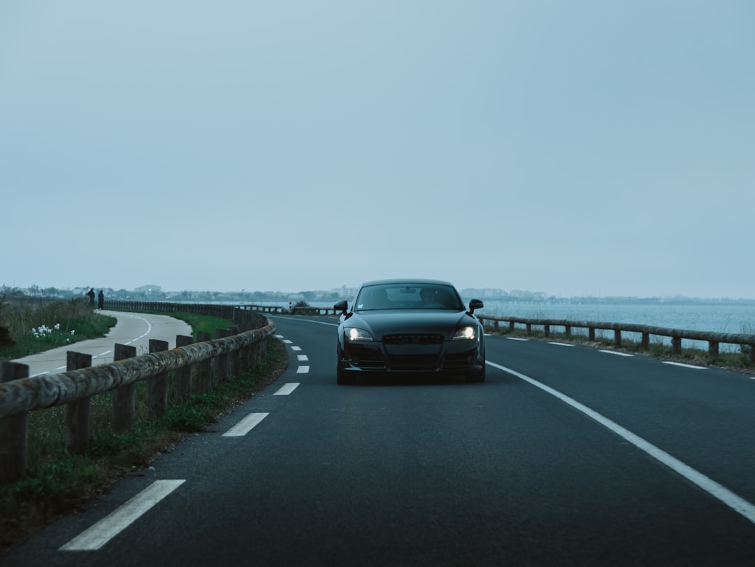 Dark car driving on a coastal road at dusk.