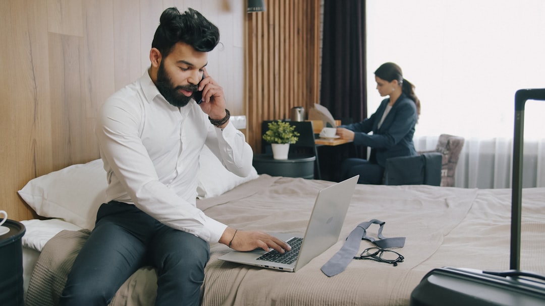 A man in a white shirt using a laptop on a hotel bed