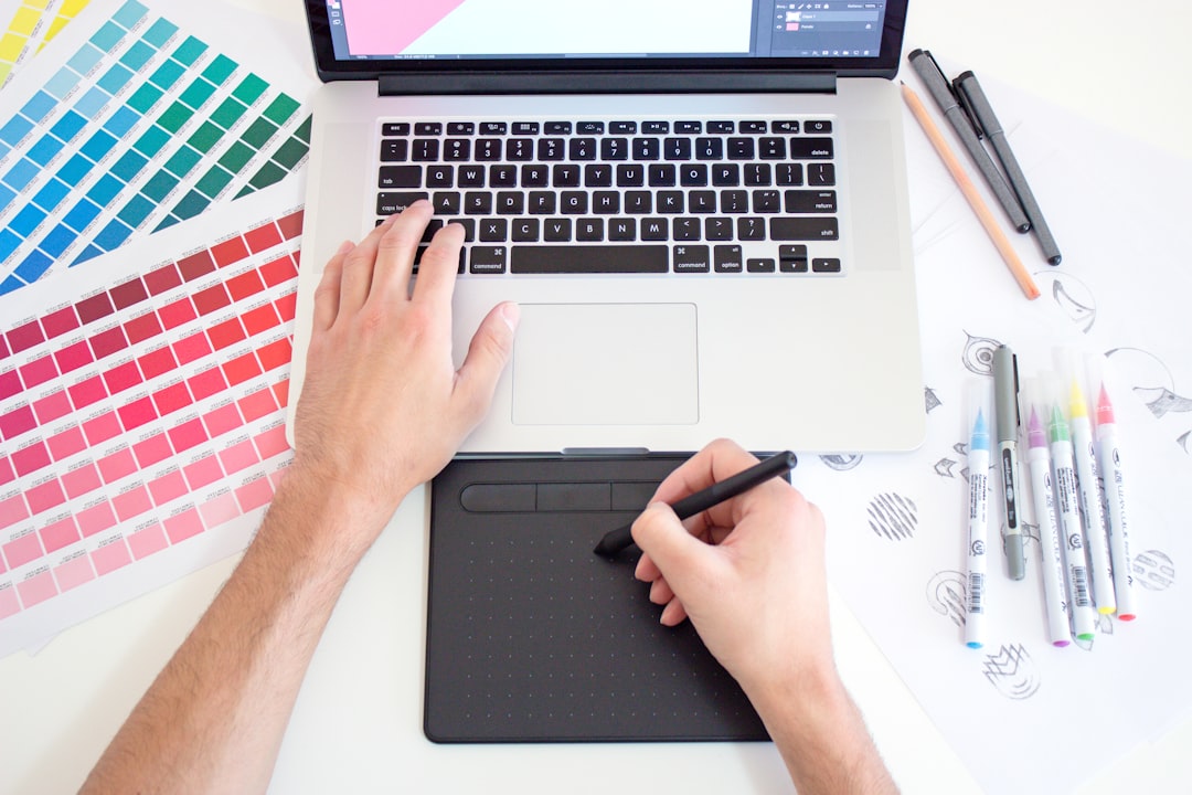 A person using a digital drawing tablet and laptop with color swatches and markers