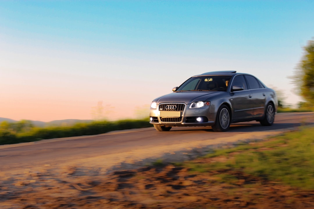 A silver sedan drives on a dirt road at sunset