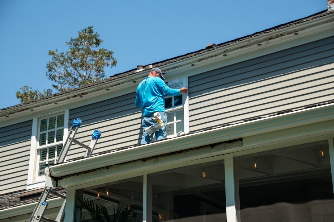 A person in a blue shirt installing window flashing on a grey house roof